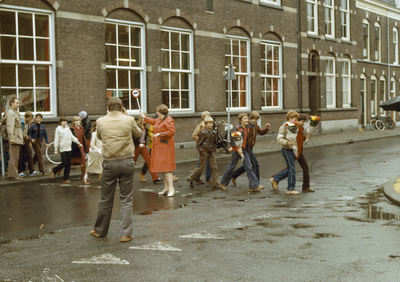 117475 Afbeelding van een verkeersbrigadier en een groep overstekende kinderen bij de R.K. basisschool St. Willibrordus ...